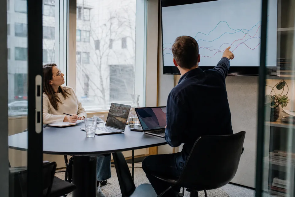 Two marketing colleagues comparing a ranking chart on a monitor in a small meeting room